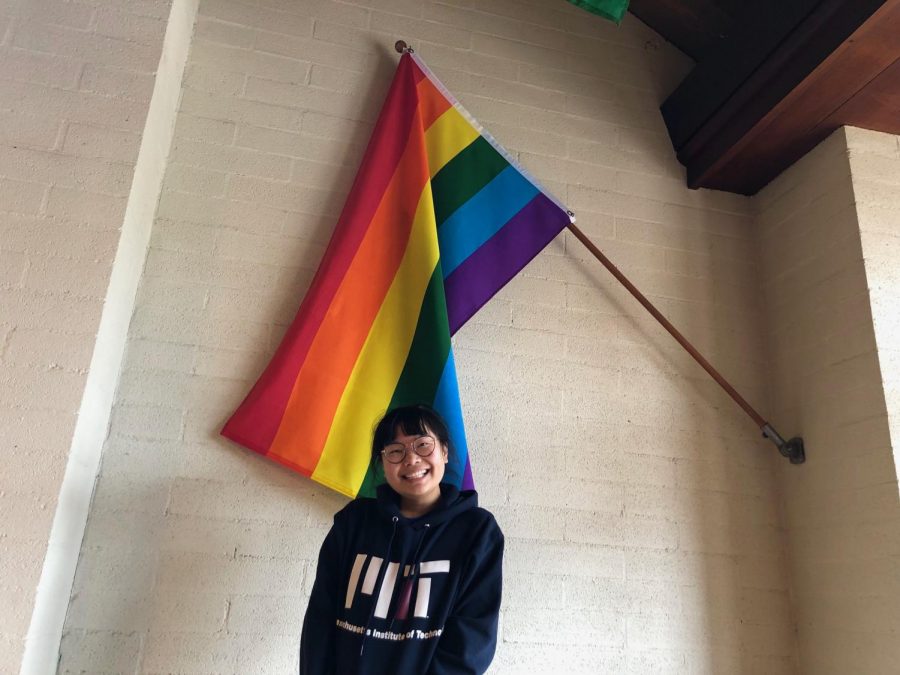 The pride flag can be found in the north corner of the Price Dining Hall. Rachel Kho (19) smiles with pride in front of it, as co-president and an ally.