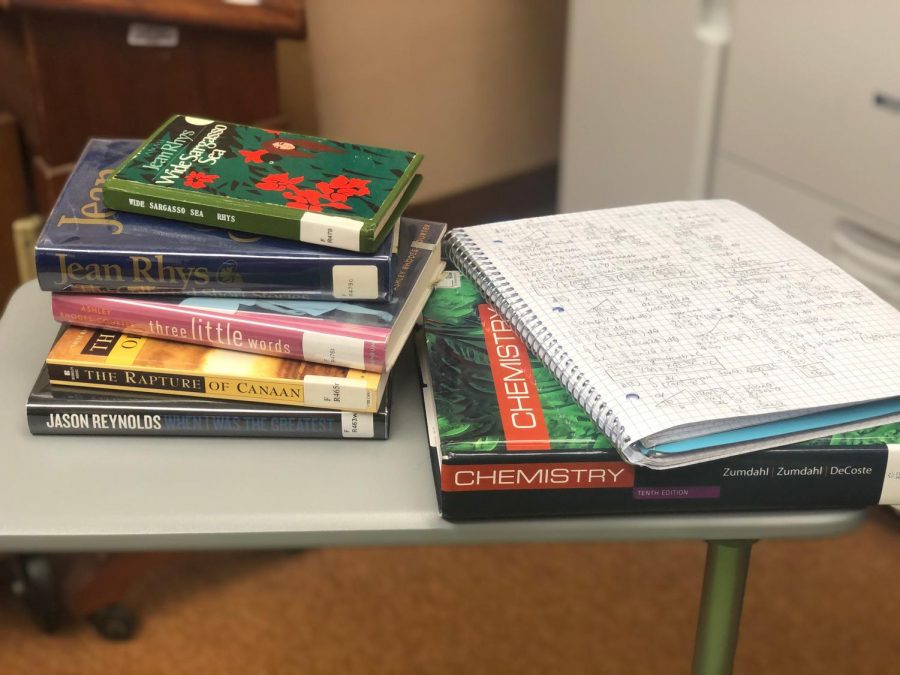 A Webbie's belongings are piled on a desk: chemistry textbook, math notebook, and five library books.