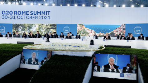 In this photo, world leaders from twenty countries attend the G20 Summit in Rome. Joe Biden, President of the United States, is representing America’s interests and discussing his main agendas. Two large screens spotlighted Biden. Other participants are tentatively listening to his speech. 