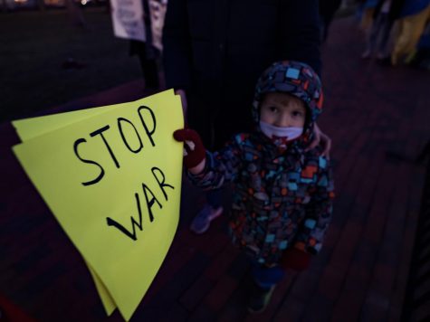 A child holds up a small neon poster written “Stop War.” Right now, Ukrainian children are forced to hide in bomb shelters or make long trips out of the major cities, or even the country, to avoid harm. 